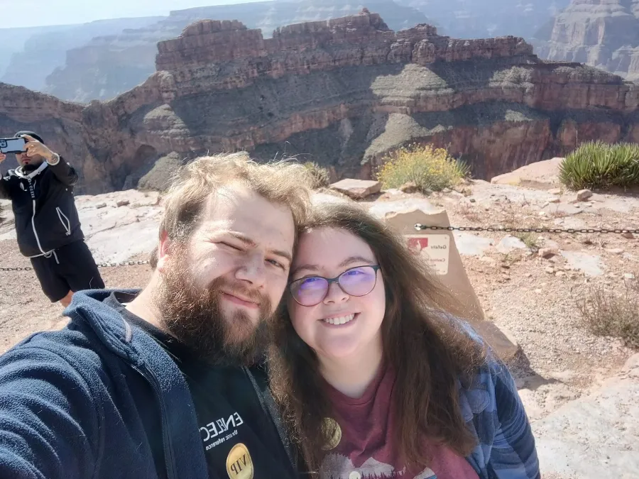 Selfie of Michelle and her husband smiling at the edge of the Grand Canyon on a sunny day.